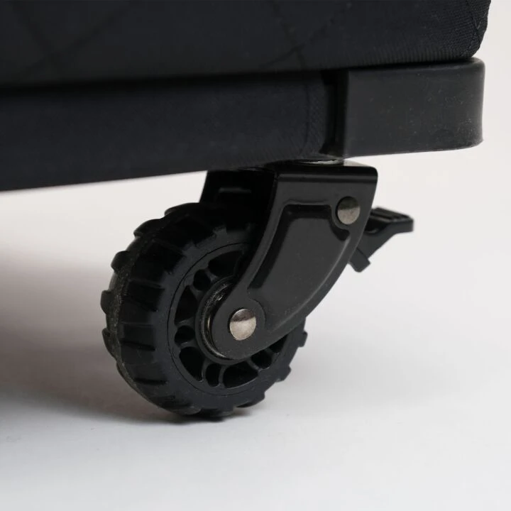 Close-up of a black caster wheel with a black plastic swivel bracket and a small silver metal screw, attached to a dark upholstered rolling bag on a white background.