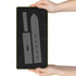 A black textured rectangular mat with a gray strap-shaped template, held by two hands against a white background.