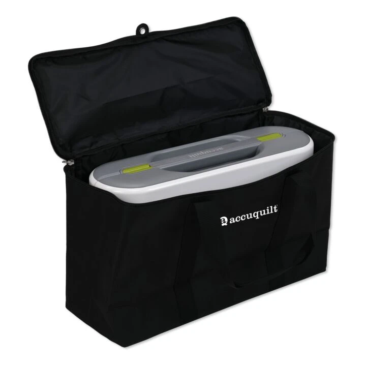 A black fabric storage bag with the lid open, containing a white and gray AccuQuilt machine. The brand name 'Accuquilt' is printed in white on the front pocket of the bag.