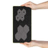 A black textured rectangular board with a thin yellow-green border, held by two hands against a white background. The board features two gray geometric hexagonal cluster designs, one smaller at the top and one larger at the bottom.
