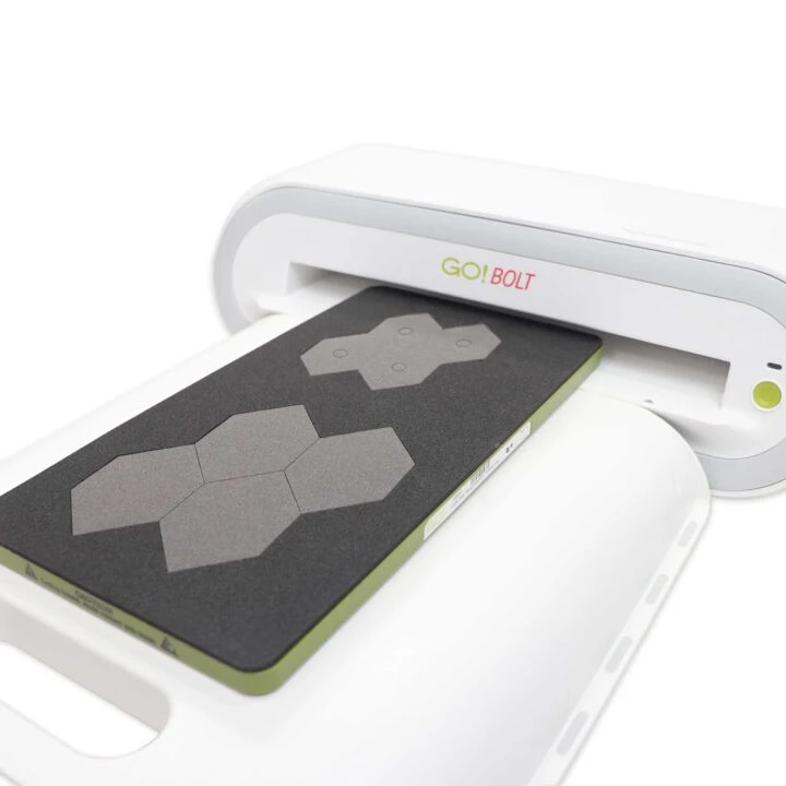 A white GO! BOLT device with a green edge, shown processing a dark gray rectangular sheet with three gray hexagonal shapes.
