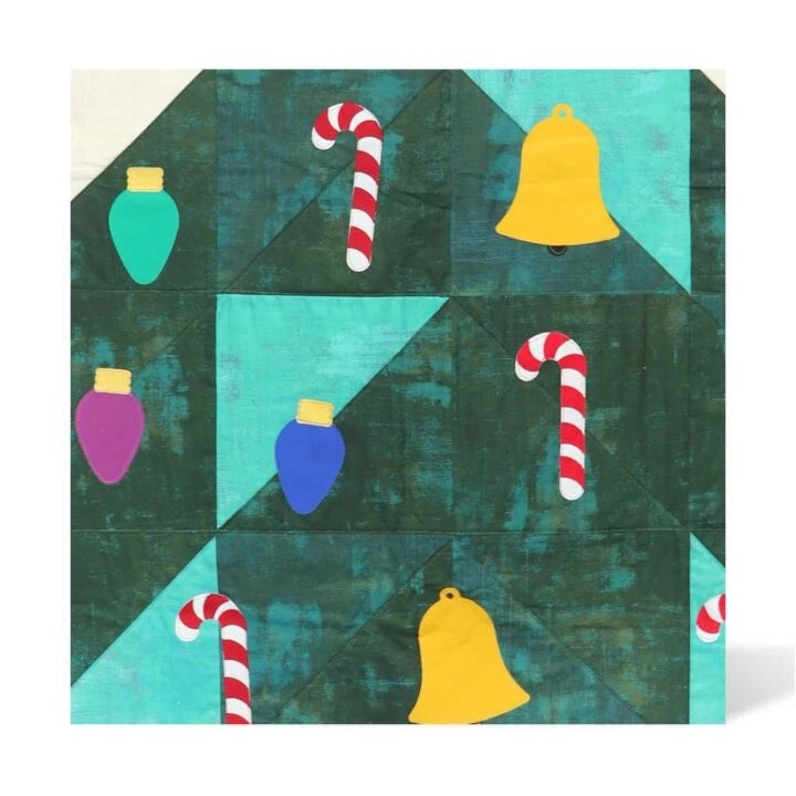 A square quilted fabric panel with a geometric pattern of dark green triangles, light teal sections, and festive holiday motifs including red-and-white striped candy canes, yellow bells, and colorful ornament shapes in teal, purple, and blue.