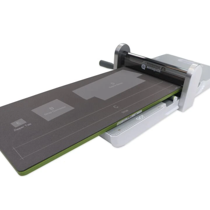 An accuquilt cutting machine shown in a clean studio shot on a white background, with a dark gray die partially ejected.
