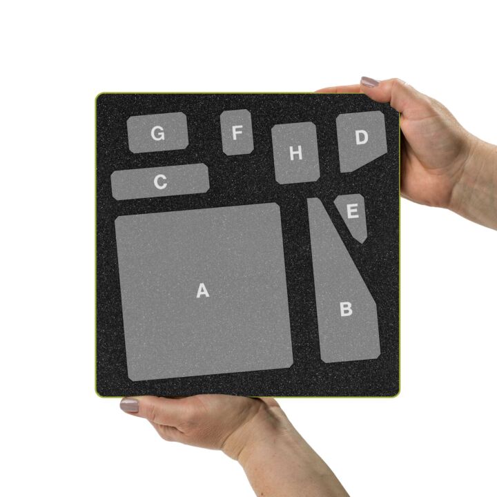 A black textured keyboard keypad mat with gray adhesive key covers labeled A through G, held by two hands against a white background.
