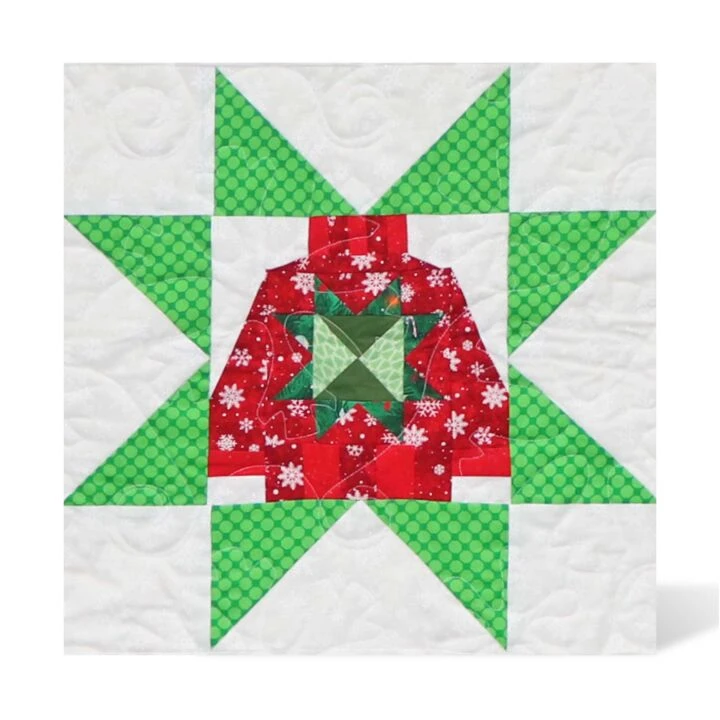 A square quilt block featuring a festive Christmas star design with a red patterned sweater motif in the center, surrounded by green patterned triangles on a white quilted background.