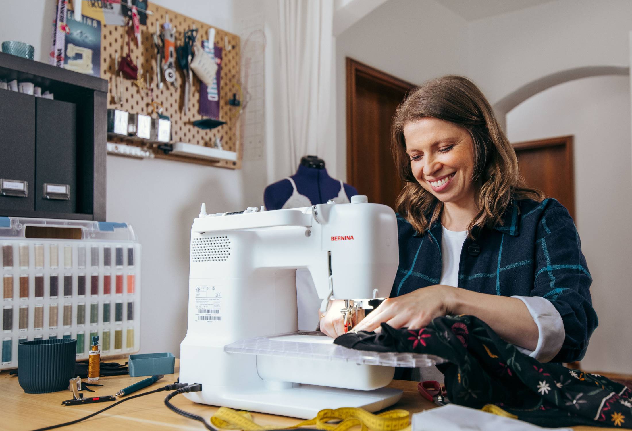 Woman using a sewing machine in a home setting with various craft supplies around.