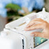 Person using a white sewing machine with a blurred background
