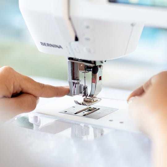 Close-up of a person using a Bernina sewing machine with a blurred background