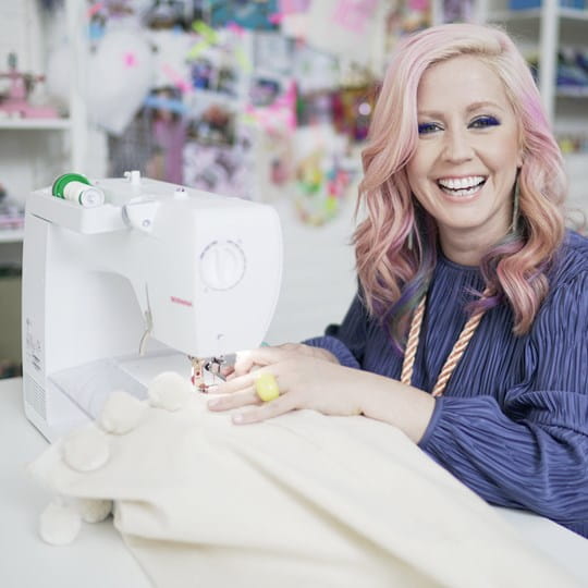 Woman with pink hair using a sewing machine in a craft store setting