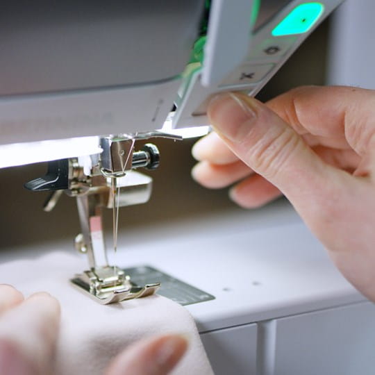 Person adjusting a sewing machine needle with close-up focus on the hand and machine.