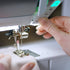 Person adjusting a sewing machine needle with close-up focus on the hand and machine.