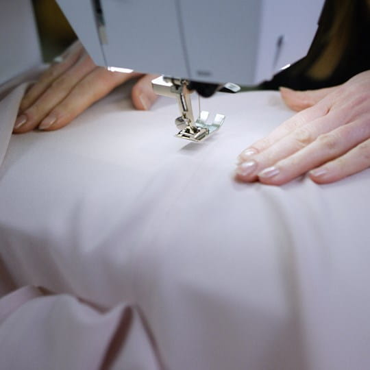 Close-up of hands operating a sewing machine on white fabric