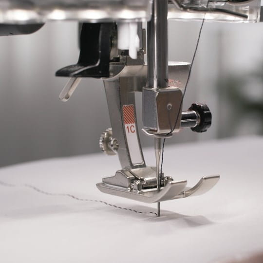 Close-up of a sewing machine needle and foot on a white fabric background