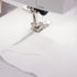 Close-up of a sewing machine presser foot stitching white fabric, showing a metallic silver presser and needle in action.