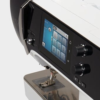 Close-up of a sewing machine with digital display and control knobs on a white background