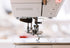 Close-up of a BERNINA sewing machine showing the needle area, presser foot, and part of the white machine body with a small red indicator light.