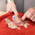 Close-up of a textured red woven textile with embroidered floral motifs in pink, white, and yellow, being held by two hands.