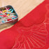 Red fabric with quilting design and a container of colorful pins on a wooden surface