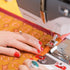 Person using a Bernina sewing machine on orange fabric with red patterns.