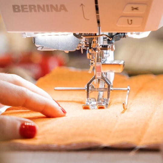 Close-up of a sewing machine needle in action with orange fabric and blurred background