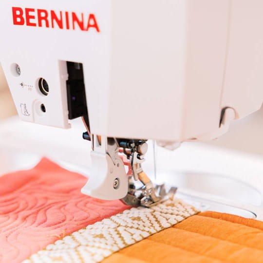 Bernina sewing machine stitching a colorful quilt with 'BERNINA' branding.