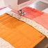 Sewing machine stitching a quilt with orange, white, and pink fabric.
