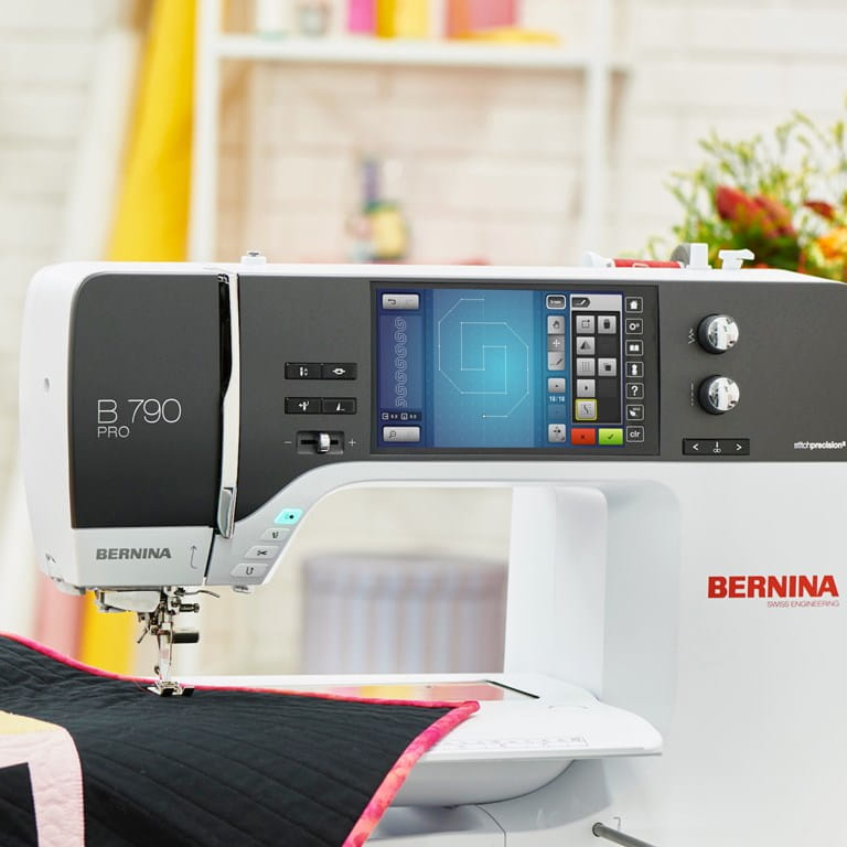 A BERNINA B 790 PRO sewing machine in white and black, shown in a bright, softly blurred sewing room setting with a quilt visible under the needle.