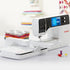 A white and black BERNINA sewing machine with a digital display screen, shown with its fabric feeddog attachment and spools of thread on a clean white surface.