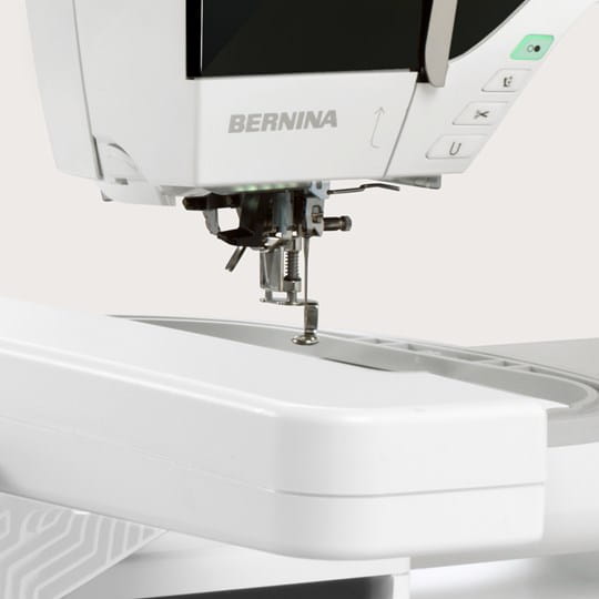 Close-up of a white BERNINA sewing machine showing the needle area, presser foot, and part of the control panel on a light neutral background.