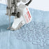Berenina stitch regulator attachment on a sewing machine needle bed with blue fabric underneath.