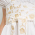 Close-up of a white dress or skirt with a wide gathered waistband tied in a bow, decorated with metallic gold floral embroidery.