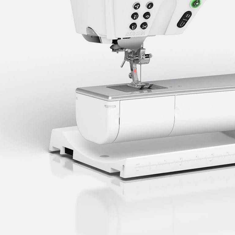 A close-up of a white sewing machine with a metallic silver presser foot and needle area, shown on a clean white studio background.