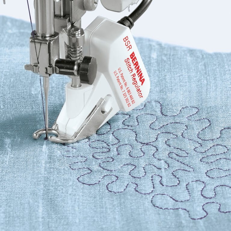 Berenina stitch regulator attachment on a sewing machine needle bed with blue fabric underneath.