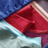 Close-up of folded cotton garments in several colors, including blue, red, pale blue, purple, and beige, showing fabric texture and stitching.
