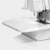 A close-up studio shot of a white sewing machine, showing the upper arm, needle area, and flat bed against a clean white background.