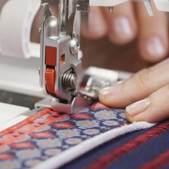 Close-up of a sewing machine needle stitching fabric with a person's hand guiding it.