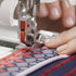Close-up of a sewing machine needle stitching fabric with a person's hand guiding it.