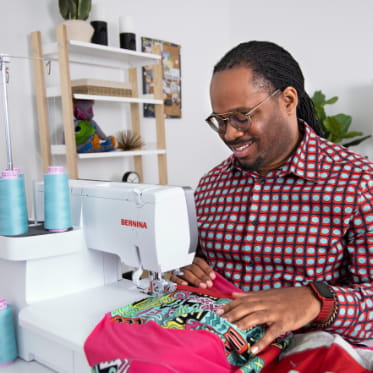 Man working on a sewing machine with colorful fabric in a home setting