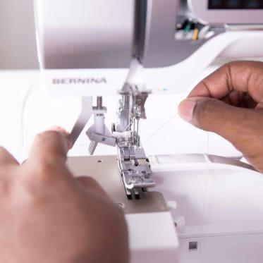 Close-up of a person's hands threading a white BERNINA sewing machine.