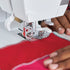 Close-up of a sewing machine in use with red fabric and hands guiding it.