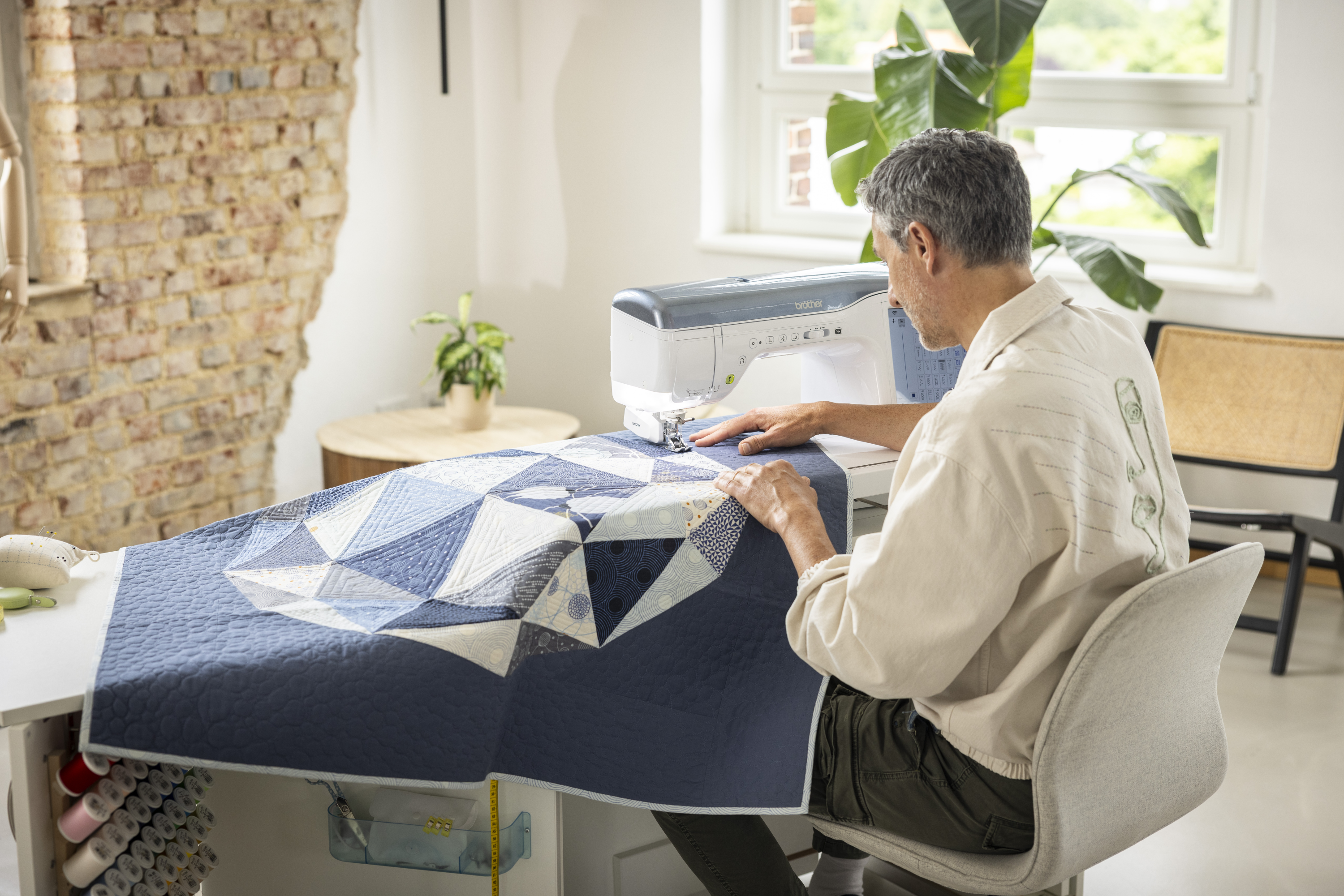 Man working on a quilt at a sewing machine in a home setting.