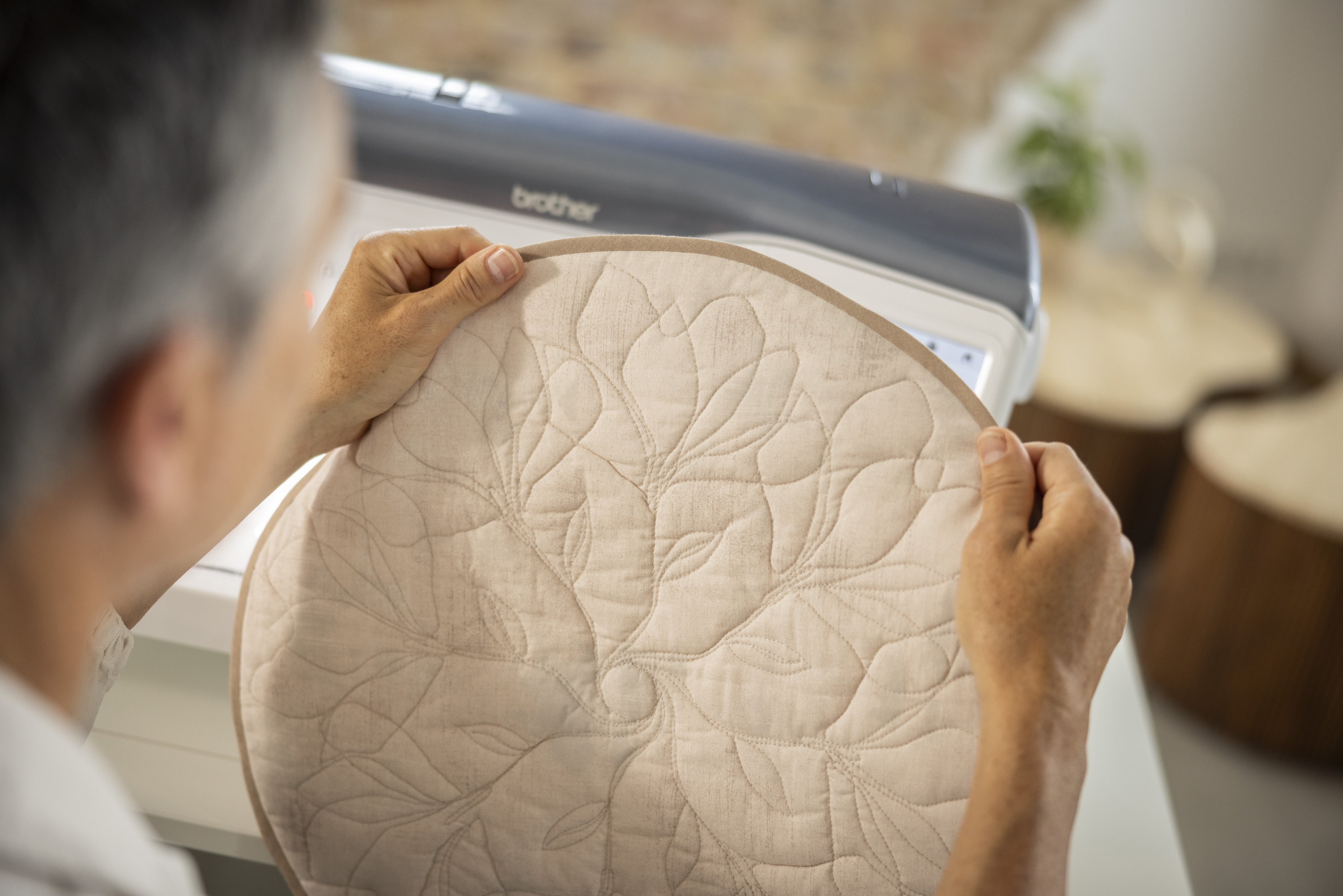 Person holding a quilted fabric piece next to a Brother machine.