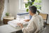 Person using a sewing machine in a home setting with a window and plant in the background