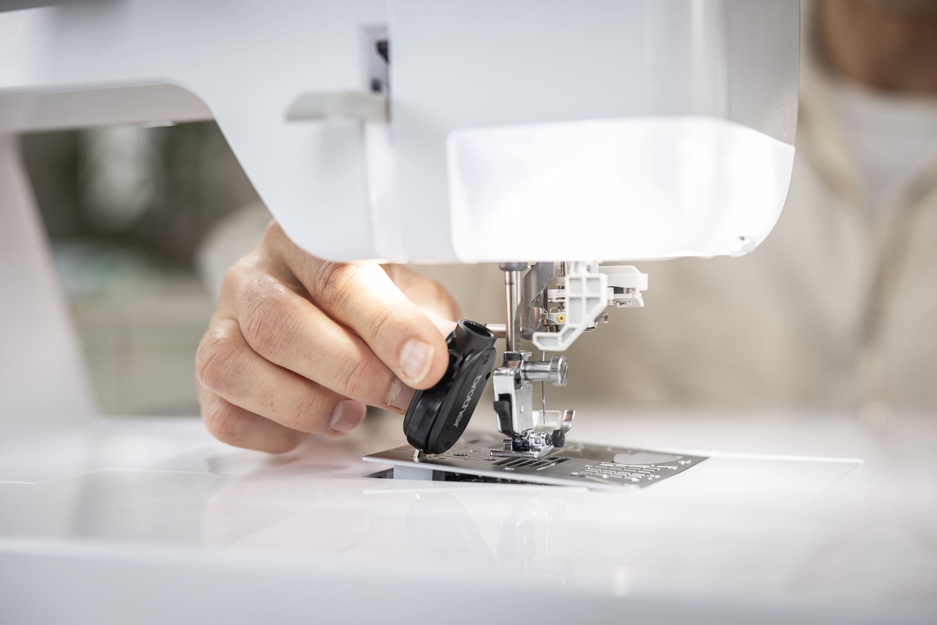 Close-up of a sewing machine with a hand adjusting the needle plate.