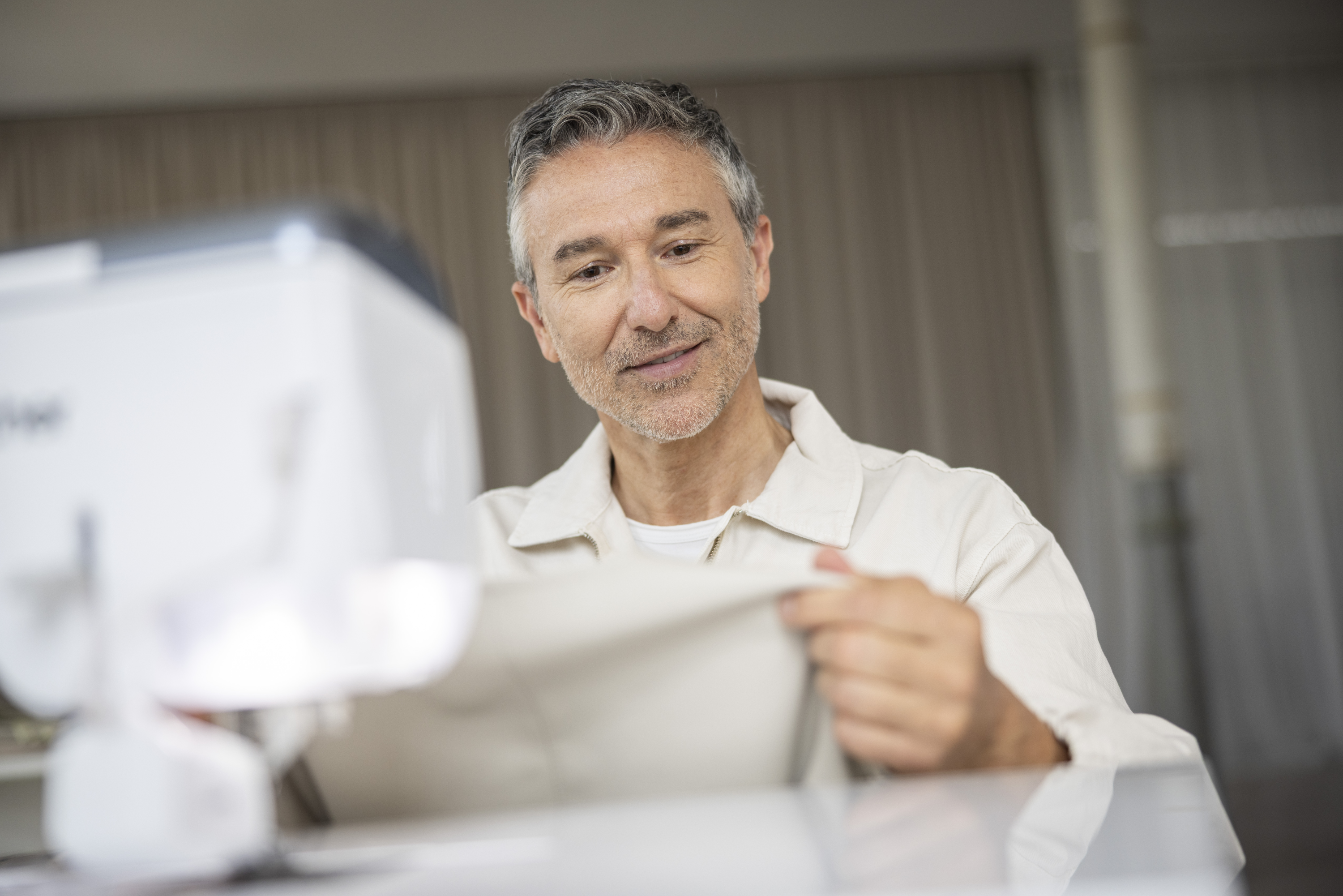 Man sitting at a desk with a sewing machine and fabric, smiling.