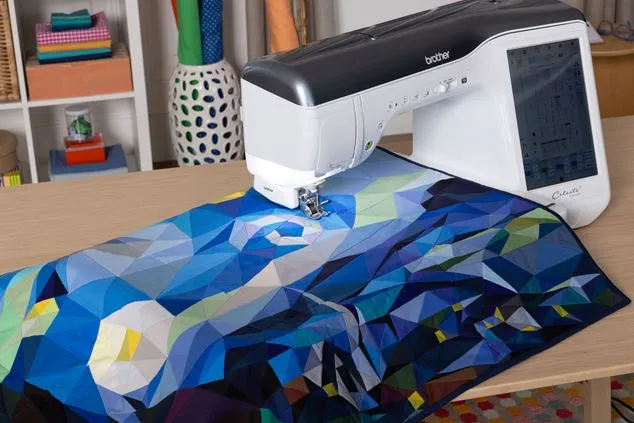 Brother sewing machine stitching a colorful fabric design on a table.