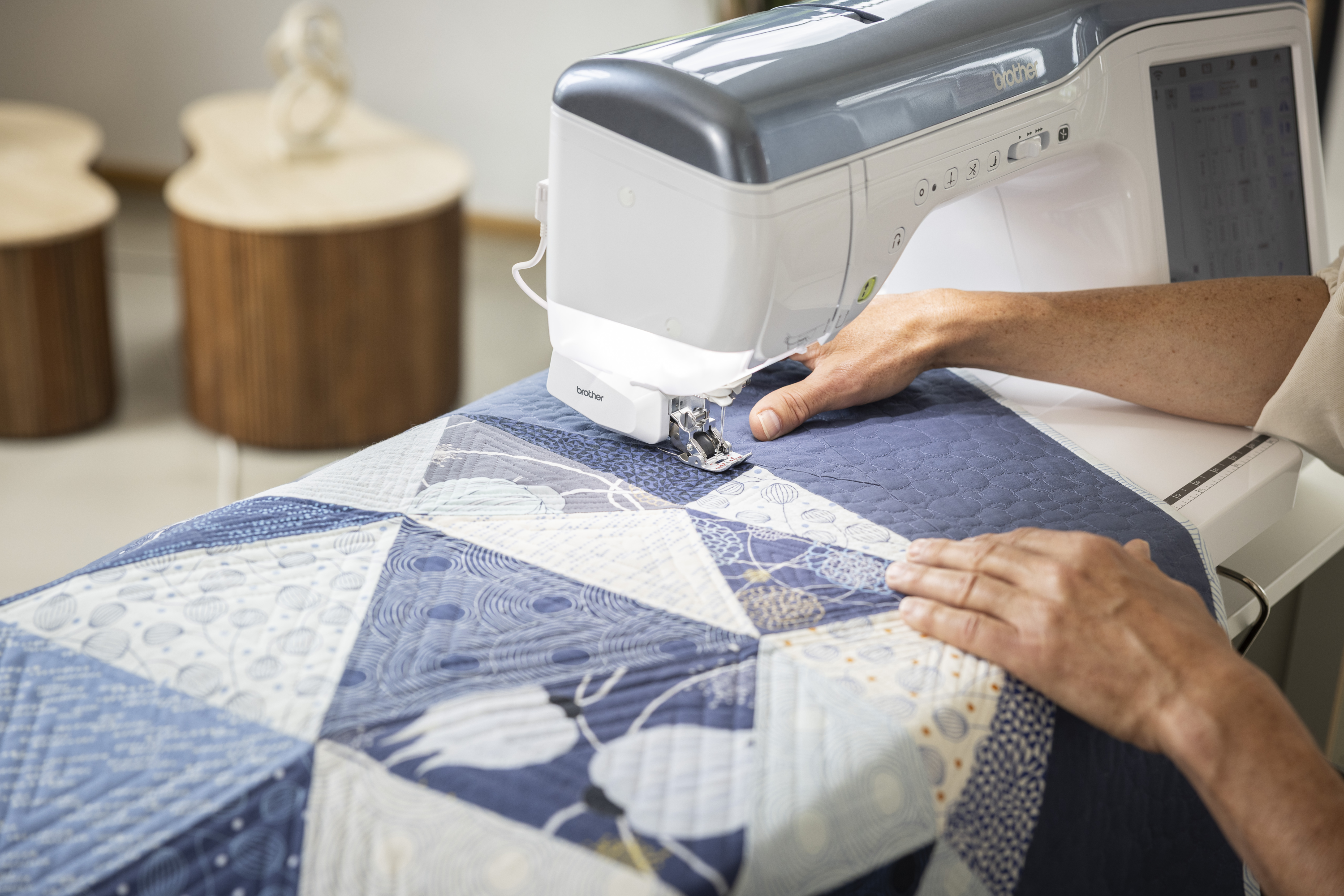 Person using a sewing machine on a quilt with wooden stools in the background