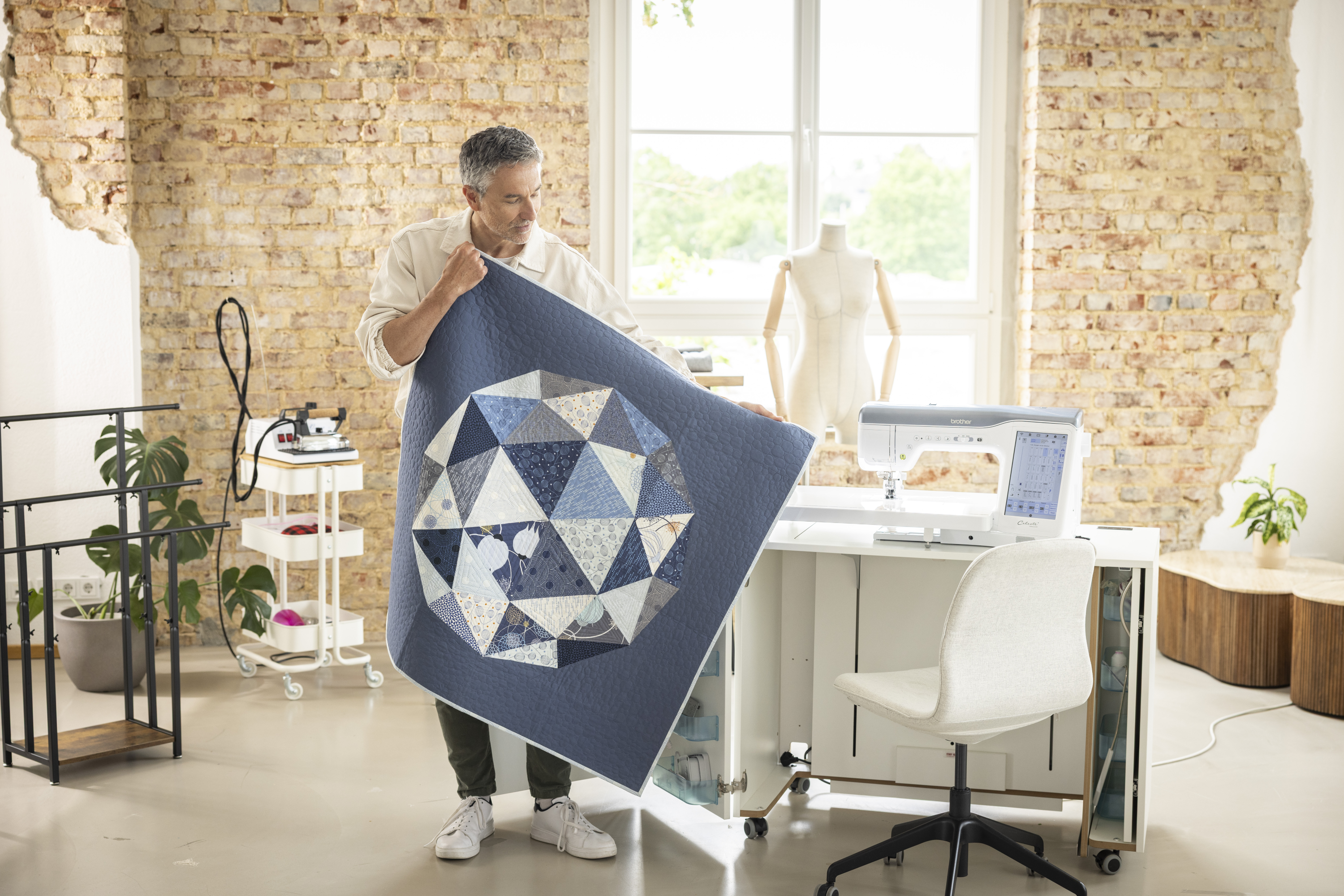 Man holding a blue quilt with geometric patterns in a modern room.