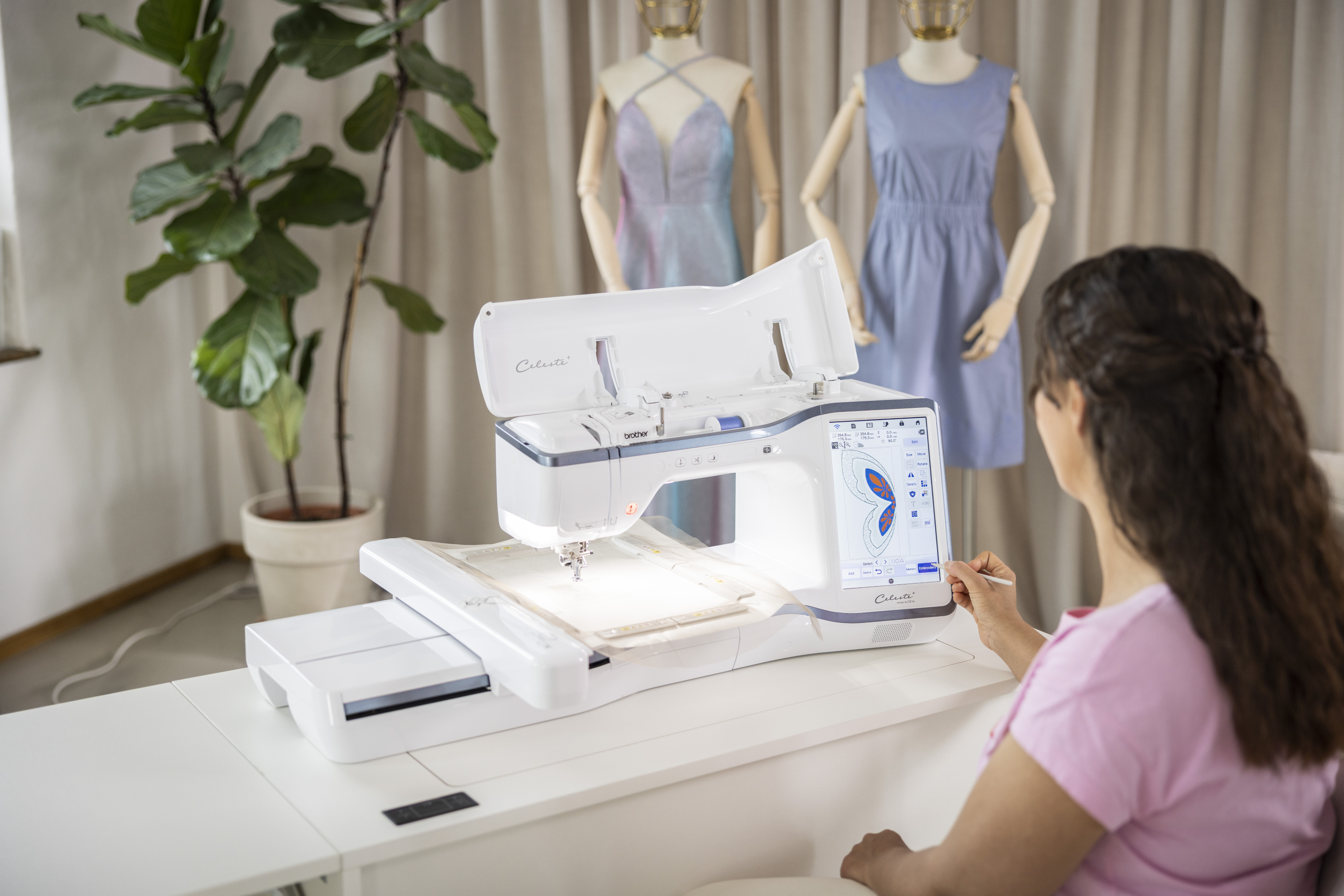 Person using an embroidery machine with mannequins and dresses in the background