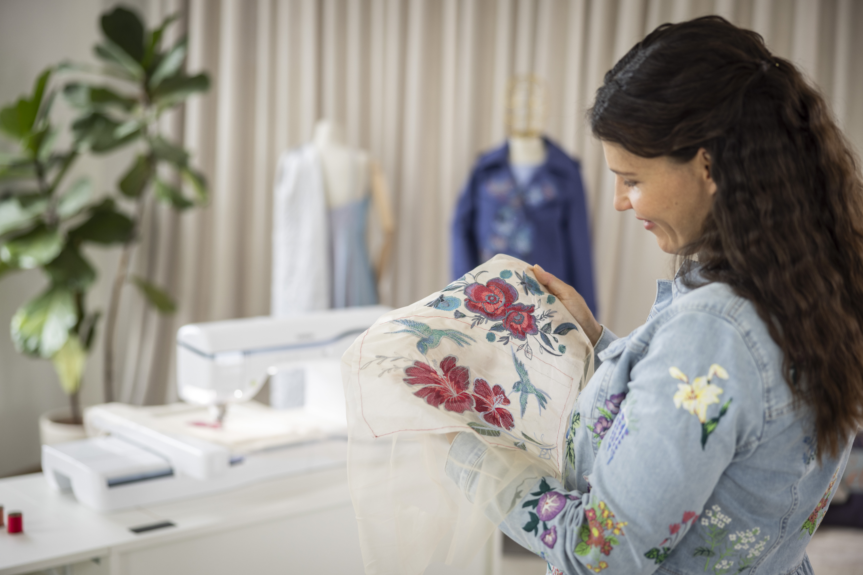 Woman holding a floral-patterned fabric in a sewing room.
